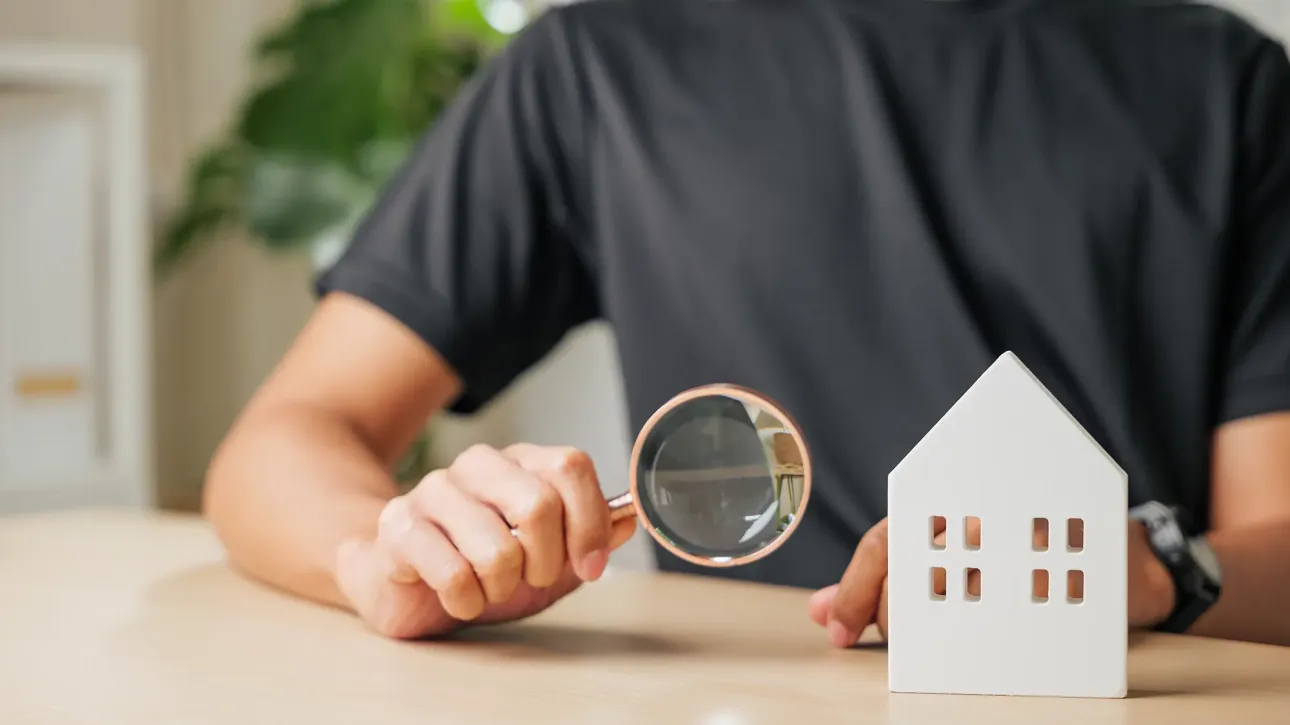 Inspector kneeling near a water heater while the buyer watches—light soft, body language relaxed, everything functioning as it should. Fix before closing.