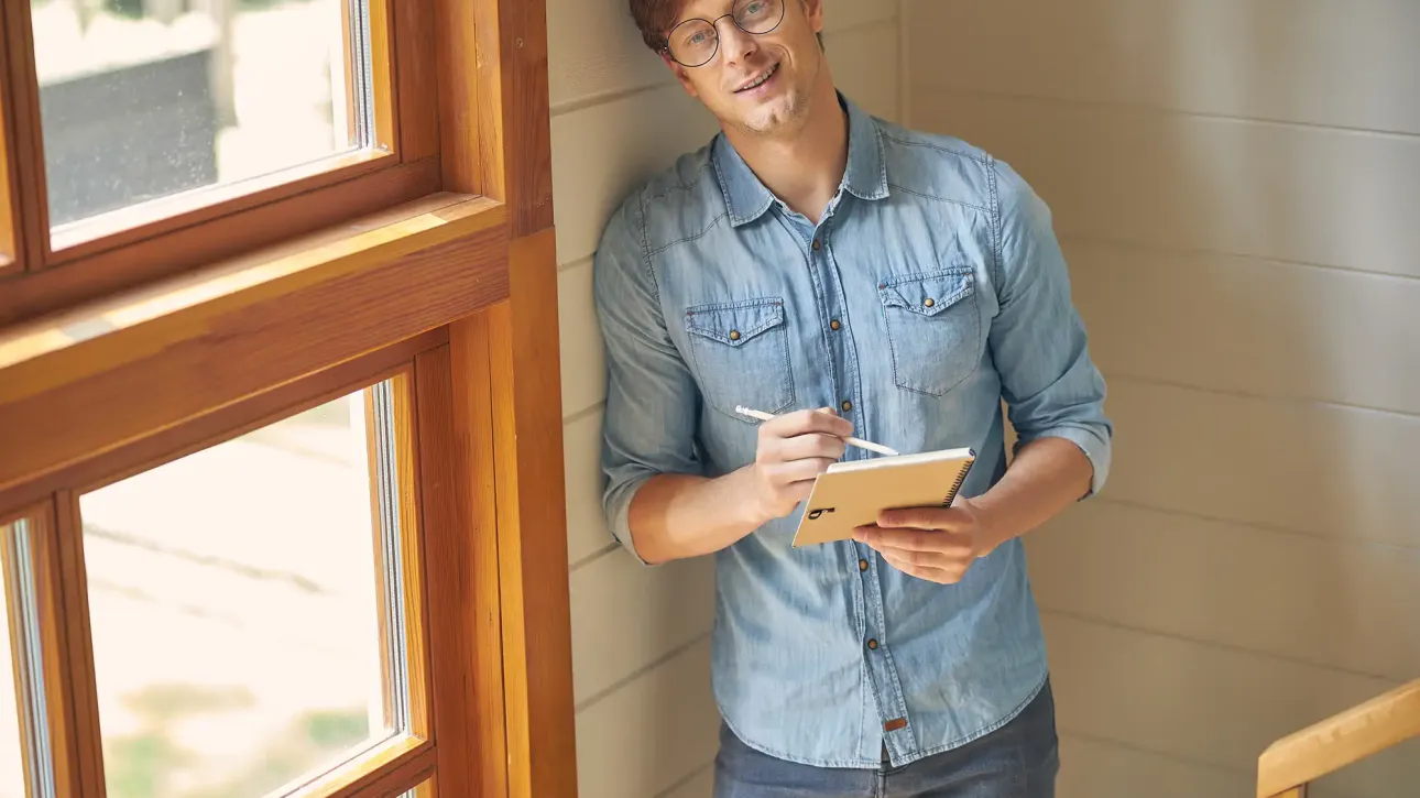 A homeowner standing in the soft afternoon light, holding a checklist near the window — a quiet moment of reflection and readiness. Fix Before Closing.